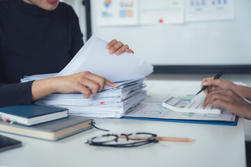 Teamwork Makes the Dream Work: Two colleagues collaborate intensely on a stack of documents, surrounded by office essentials, symbolizing dedication and shared workload.