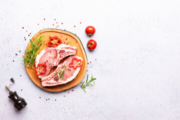 Raw pork chops ready to cook with spices, herbs and vegetables on light marble table top view, copy space for your text.
