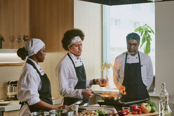 Male cook cooking steak in flambe style while his colleagues looking at flame