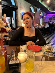 Millennial woman enjoying a pleasant evening at a lively restaurant, seated at a table with a red plate and warm candlelight. Atmosphere is night with a mix of modern and cozy interior design