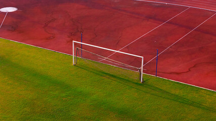 A dynamic aerial view of a soccer goal post on a lush green field adjacent to a vibrant red running track, capturing the essence of outdoor sports and athletics
