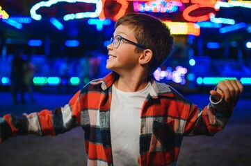 Fototapeta premium A cute boy happily spends time in an amusement park. Concept of happy childhood and holidays.