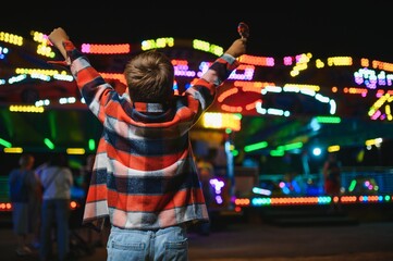 A cute Caucasian boy, a child, came to the amusement park to have fun, play and ride a merry-go-round. A child standing in front of a merry go round