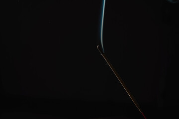 Incense burning smoke fumes and wisps. Burning aromatic incense smoky stick for meditation and relaxing. Aromatherapy smokes for yoga. Aroma sticks smoke on black background with white backlit.