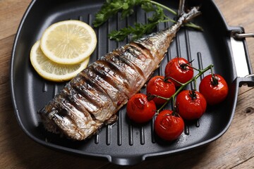 Delicious grilled mackerel, tomatoes, parsley and lemon in pan on wooden table, closeup