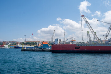 Cargo ships docked at a busy harbor with cranes and a clear blue sky in the background during midday
