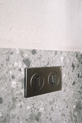 Light switch is mounted on a textured wall featuring gray stone tile