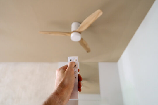 Person using remote control to adjust ceiling fan in living room