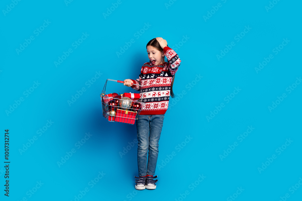 Wall mural Photo of shocked excited cute girl wear ugly print sweater hold christmas decoration isolated on blue color background