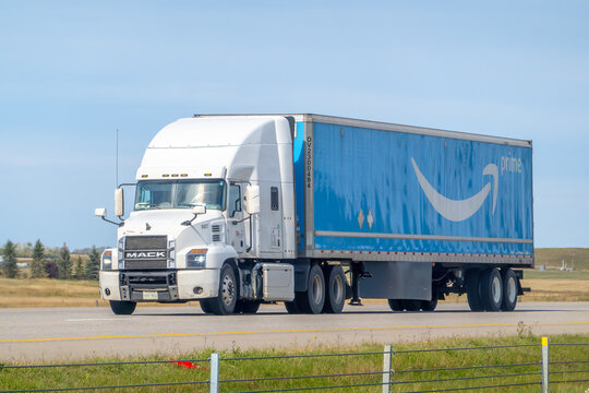Calgary, Alberta, Canada. Oct 2, 2024. A white semi truck hauls a large blue Amazon Prime trailer down the highway, featuring the iconic Amazon smile logo and streamlined design.