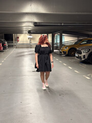 Millennial woman in a black dress walks through an empty parking garage, her pink sneakers adding a pop of color. Setting is urban and modern, with cars lined up neatly in the dimly lit space