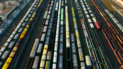 Fototapeta premium Aerial view of a busy train yard with numerous freight cars. A high-angle aerial shot of a large train yard filled with rows of freight cars in various colors and types.