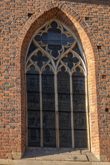 Gothic-style arched window with stained glass on a brick church wall in the afternoon sunlight. Concept of historical architecture, religious buildings, and decorative design elements