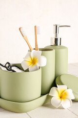 Composition with set of bath supplies and plumeria on white tile table