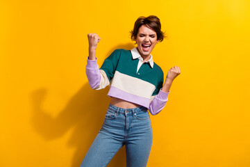 Portrait of pretty nice young girl raise fists attainment wear shirt isolated on yellow color background