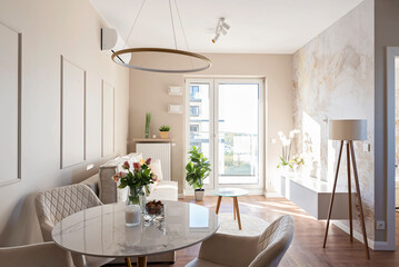 Modern living room with round table and design chair on wooden floor and window in new apartment. Light in room and wallpaper on the wall. Real estate.