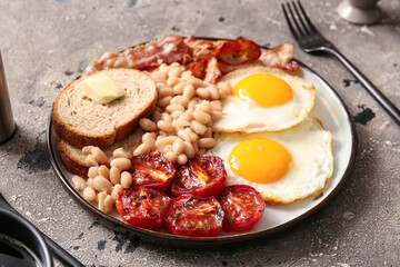 Plate of tasty English breakfast with fried eggs on grey background