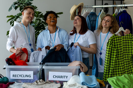 Group of volunteers, young women and man, sorting clothes in charitable foundation for charity donation, recycling. Concept of textile pollution, conscious consumption. Ecology, sustainable lifestyle