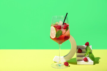 Glass of fresh raspberry mojito and decorative podium with berries on colorful background