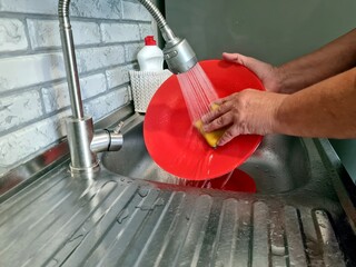 woman washes dishes, tap water pours onto a red plate