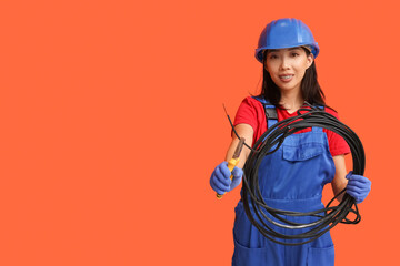 Young female electrician with pliers and cables on orange background