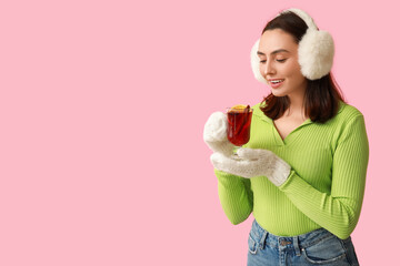 Beautiful young woman with glass cup of hot mulled wine on pink background