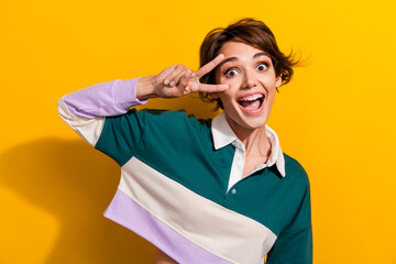 Portrait of pretty nice young girl show v-sign eye good mood wear shirt isolated on yellow color...