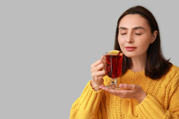 Beautiful young woman with glass cup of hot mulled wine on grey background