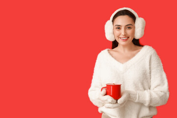 Beautiful young woman in warm mittens with cup of hot mulled wine on red background