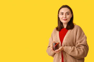 Young woman with glass cup of hot mulled wine on yellow background