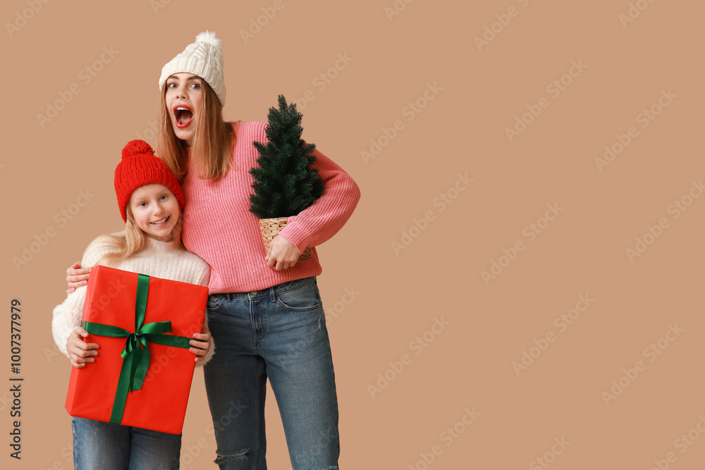 Poster Cute little girl with gift box and her mother holding small Christmas tree on brown background