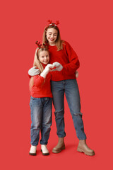 Cute little girl and her mother in reindeer horns showing heart gesture on red background