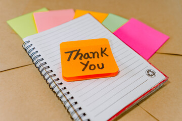 Thank you phrase written on recycled cardboard with a background of a lined notebook and post-it notes