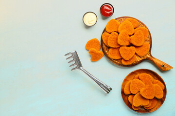 Wooden board and plate with tasty nuggets in shape of heart on light blue background. Valentine's Day celebration