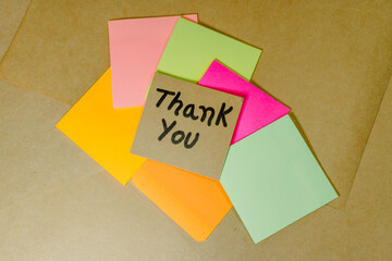 Thank you phrase written on recycled cardboard with a background of a lined notebook and post-it notes