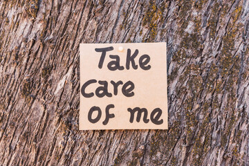 Take care of me written and drawn on recycled cardboard with a textured background made of tree bark