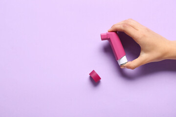 Child's hand with asthma inhaler on lilac background