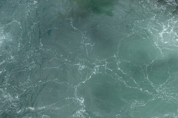 Obraz premium Detailed close-up of a turbulent green ocean water surface, showing swirling patterns, textures, and white foam on the waves.