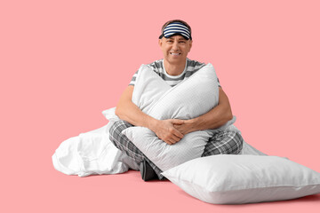 Handsome mature happy man in stylish pajamas with pillows and blanket on pink background