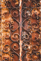 A rusted iron gate with a lot of detail, including a lot of swirls. The gate is old and worn, giving it a sense of history and character. The rusted appearance of the gate adds to its overall mood