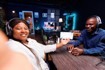 African lady filming podcast with guest telling listeners an engaging narrative using selfie camera...