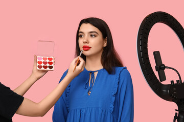 Female makeup artist working with young woman while recording video on pink background