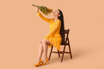 Beautiful young woman with bouquet of mimosa flowers sitting on chair against beige background