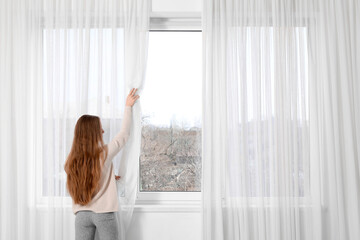 Young woman closing tulle in light modern flat