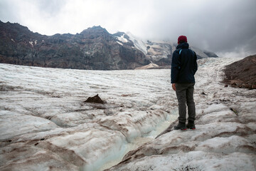 Eroded Elegance of mount Kazbegi: A trekker stands on a snowy slope, mountain range and clouds creating a breathtaking backdrop.