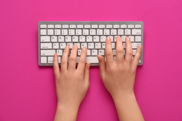 Female hands typing on keyboard on pink background