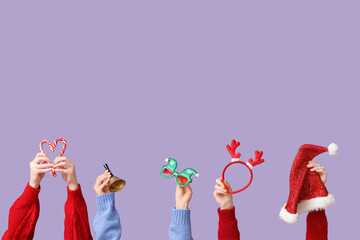 Female hands holding Christmas reindeer horns headband with Santa hat, bell and candy canes on lilac background