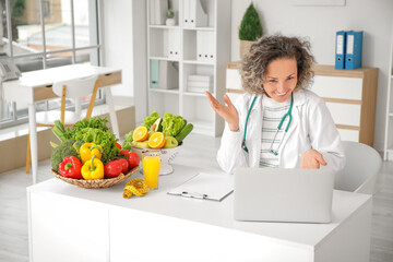 Mature female nutritionist with laptop video chatting at table in office