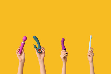 Female hands with different vibrators on yellow background