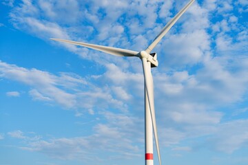 Fototapeta premium A stunning white windmill towers against a bright blue sky filled with soft, fluffy clouds. Its large blades rotate gently, representing the beauty and efficiency of renewable energy harnessed from